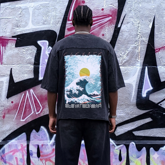 Person wearing a black shirt with a graphic design on the back, standing in front of a graffiti-covered wall.