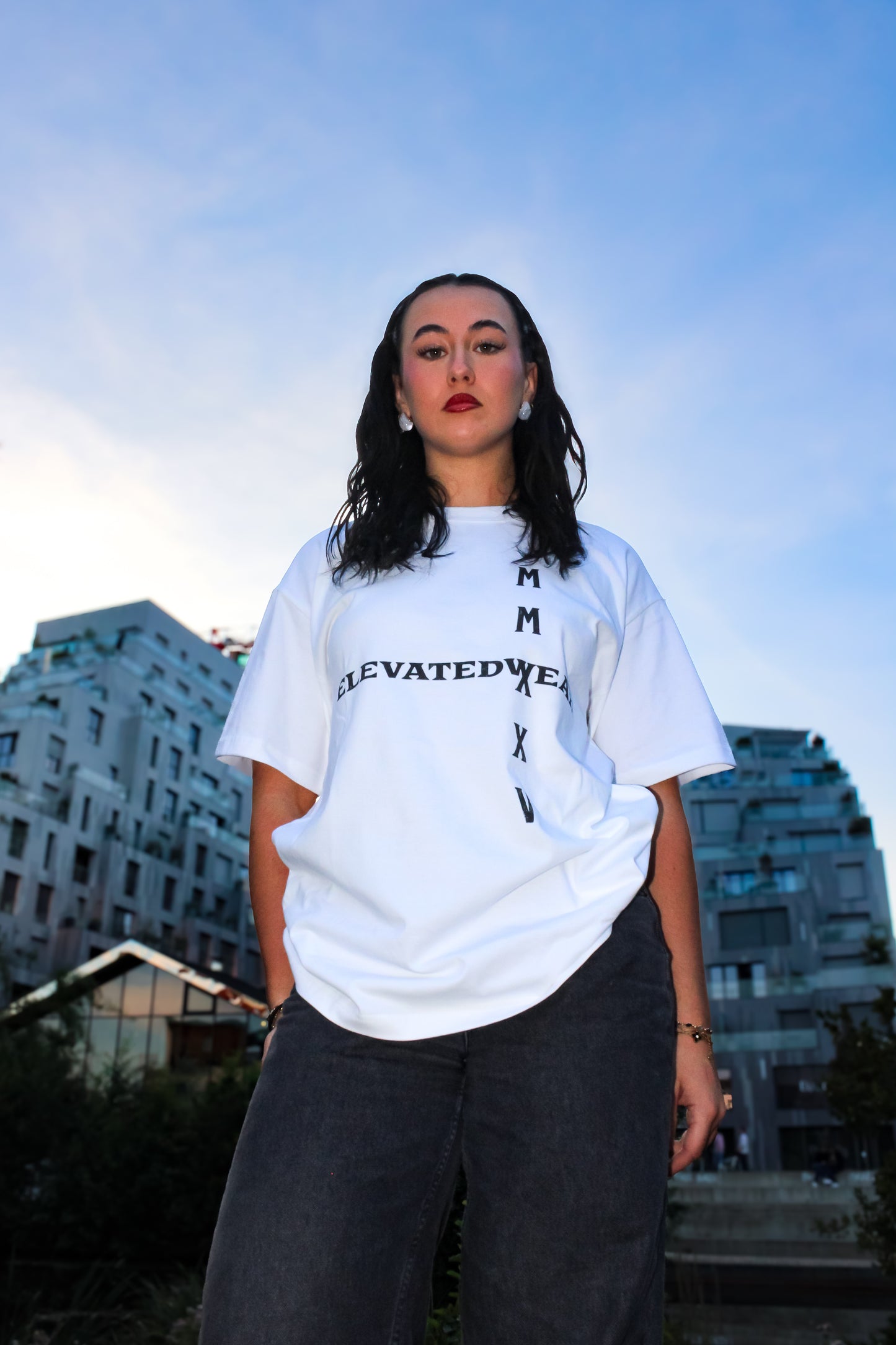 Person wearing a white t-shirt with text, standing outdoors with buildings in the background