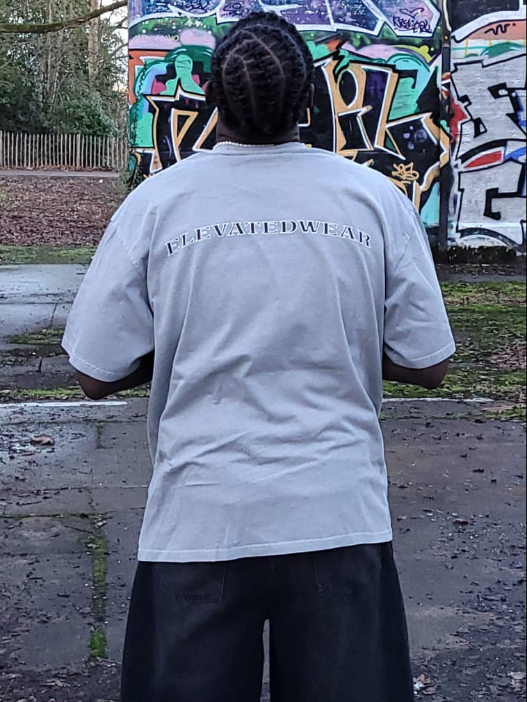 Person wearing a light gray t-shirt with text, standing in front of a graffiti-covered wall.